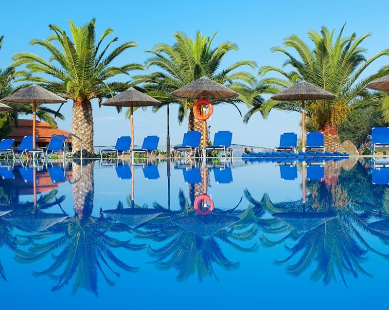 Pool mit Palmen, Liegestühlen und Sonnenschirmen im Blue Dolphin Hotel ****